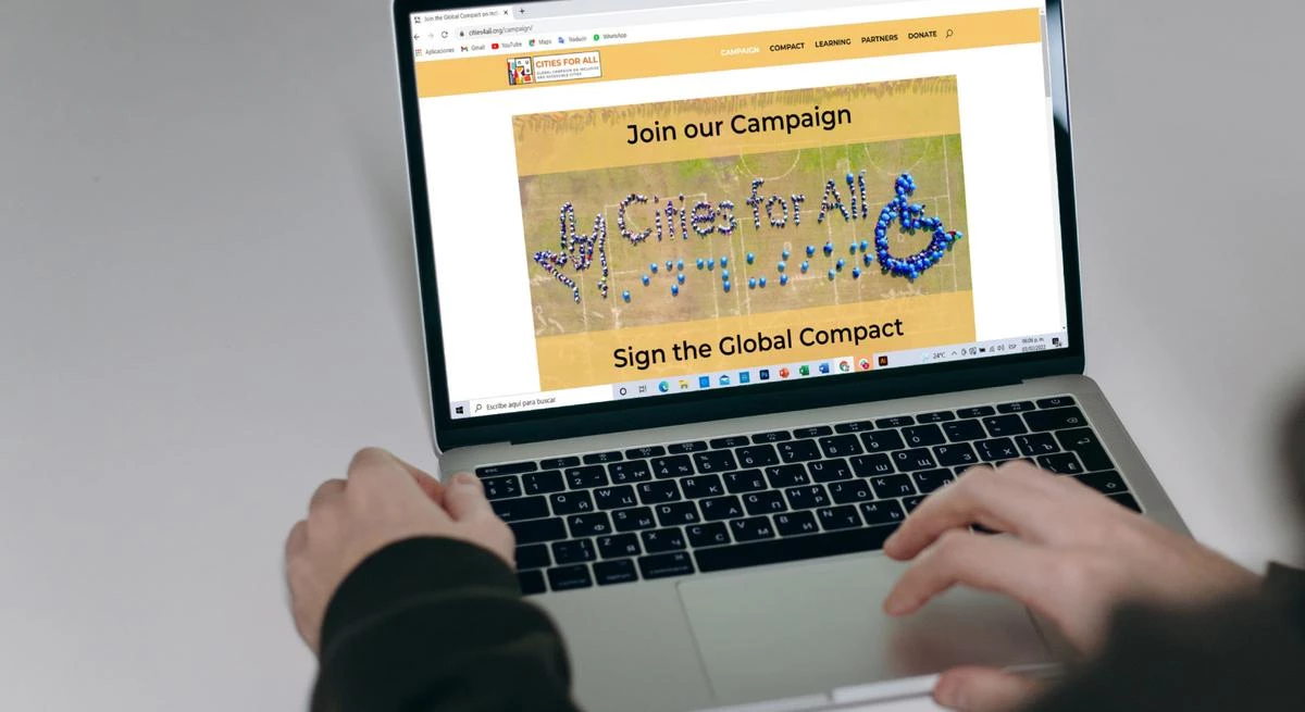 Person using a laptop to view a Cities for All campaign page about signing the global compact