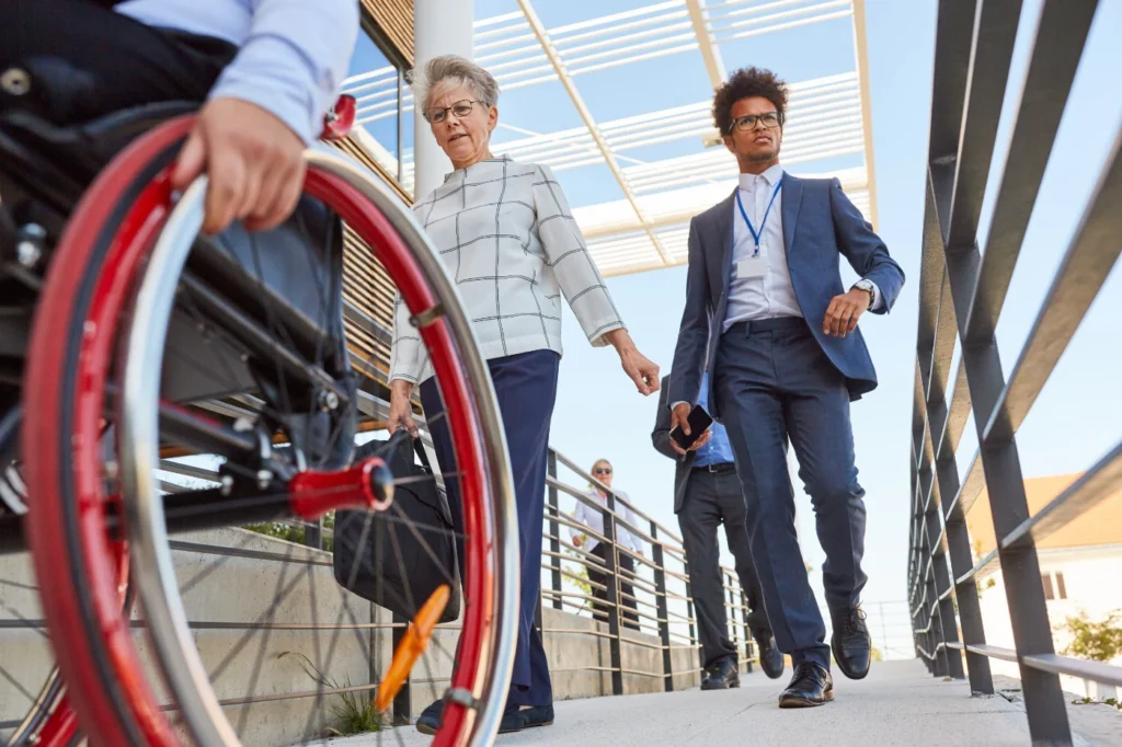 A group of professionals walking on an accessible ramp, with a wheelchair wheel visible in the foreground.