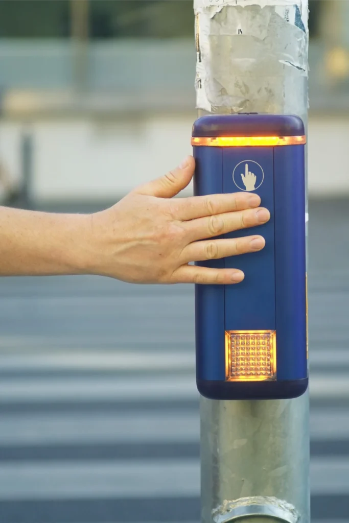 A hand pressing an accessible pedestrian crossing button with warning lights