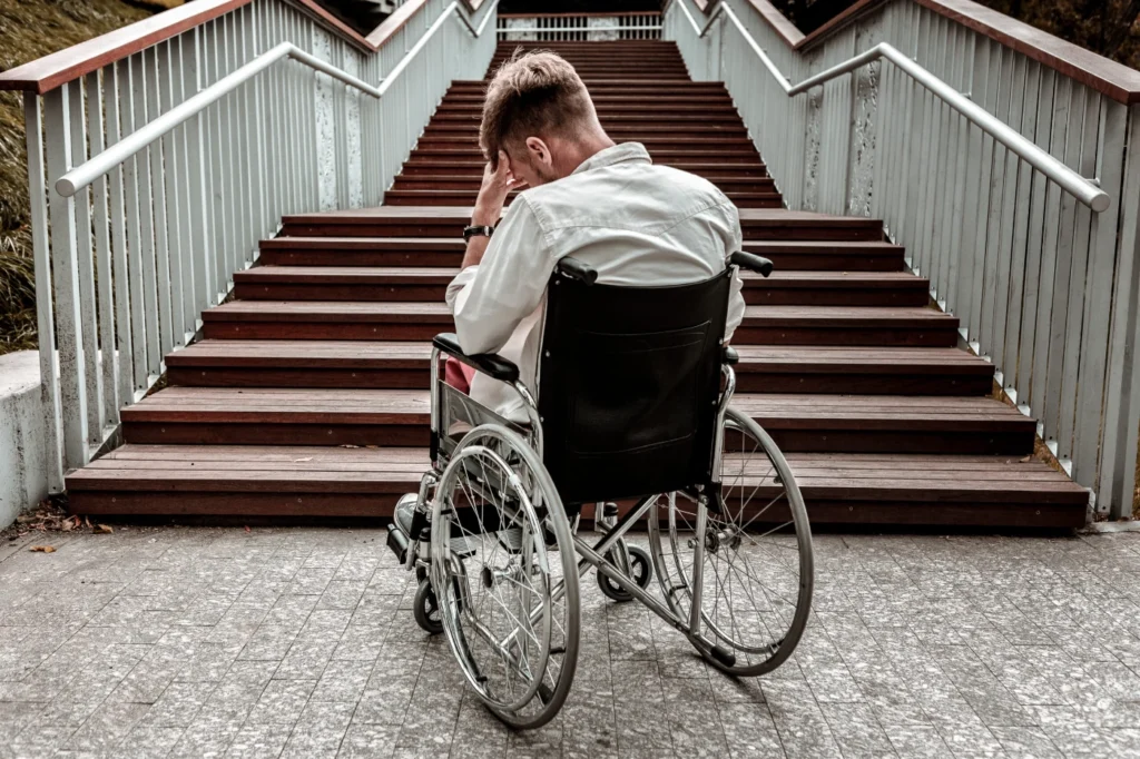 A wheelchair user facing a large staircase, which suggests an accessibility barrier
