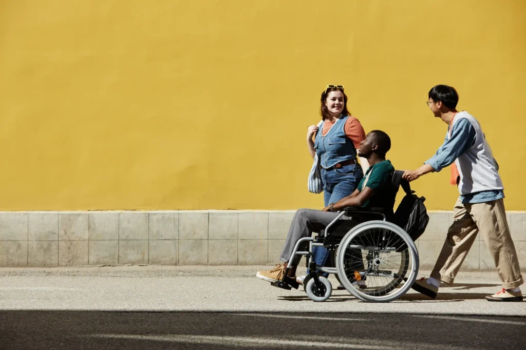 Friends walking together outdoors with a wheelchair user against a yellow wall