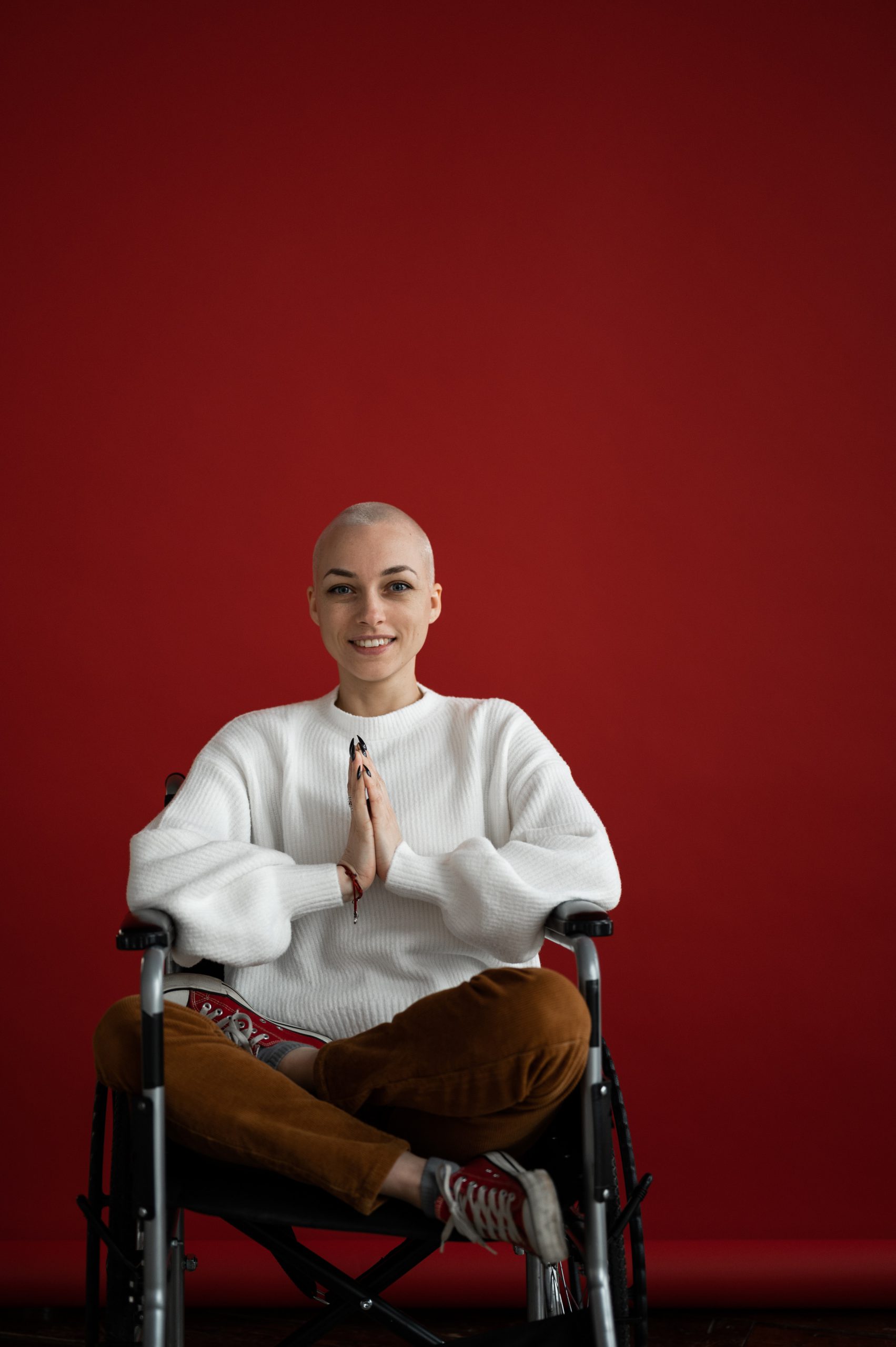Person seated in a wheelchair against a red background with hands together.