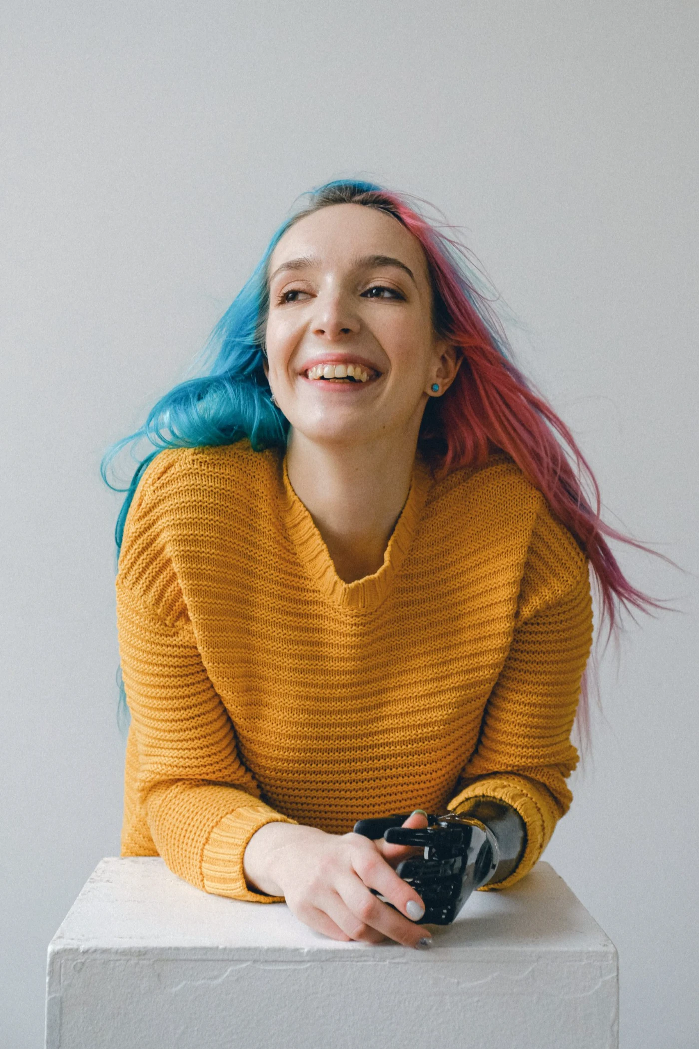 Smiling person with colorful hair and a prosthetic arm wearing a yellow sweater