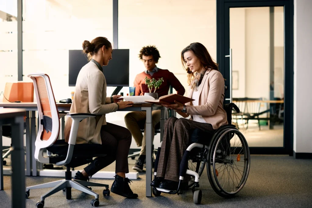 Wheelchair user reviewing documents with a colleague in a modern office.